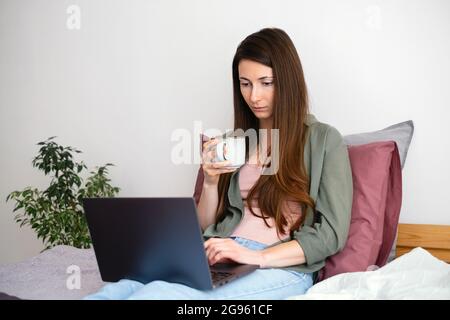 Young woman freelancer working from home with laptop and drinking coffee. Typing keyboard. work from home. Slow life concept. Stock Photo