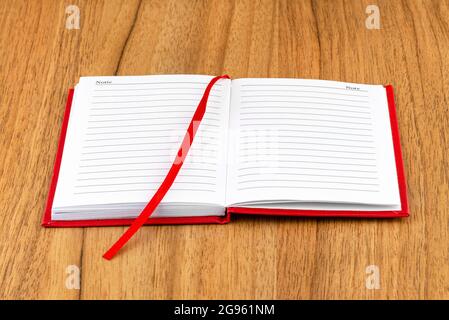 Open red lined notebook lying on a wooden table with a visible ribbon. Stock Photo