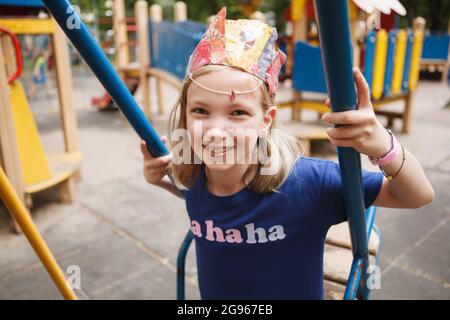 Charming happy child smiling to the camera, sitting on a swing on playground Stock Photo
