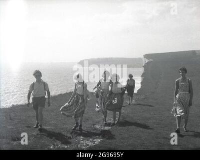 1950s, historical, summertime members of a rambling club, the women in long skirts, walking along the top of Beachy Head', a famous chalk headland on the South Downs at Eastbourne, East Sussex, England, UK. The highest chalk sea cliff in Britain, its surrounding undulating downs are a beautiful spot for pleasure walking, with views over the English Channel. An area of outstanding natural beauty, in 1929, by an act of Parliament, the land was purchased to safeguard its use for future generations Stock Photo