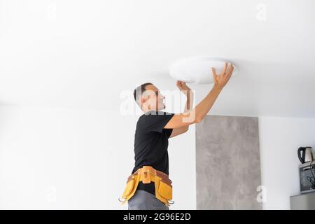 Worker repairing lamp on stretch ceiling indoors Stock Photo