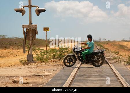 Uribia, La Guajira, Colombia - May 28 2021: Indigenous Youth Riding a Motorcycle without a Helmet on the Railroad Tracks in the Desert Stock Photo