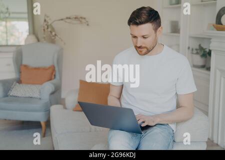 Serious young man using laptop computer for remote work from home Stock Photo