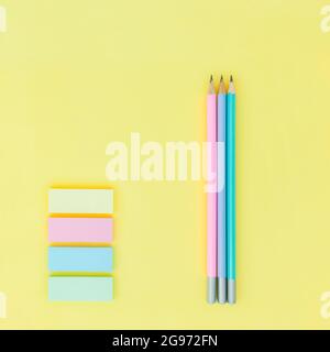 Three colored lead pencil and pastel colored sticky notes on yellow paper background Stock Photo