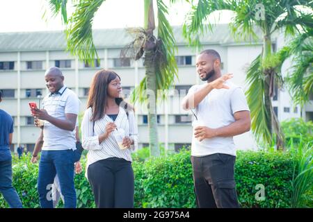 African friends consisting of a guy and a lady interacting together with their friend chatting on phone beside them in a beautiful outdoor park Stock Photo