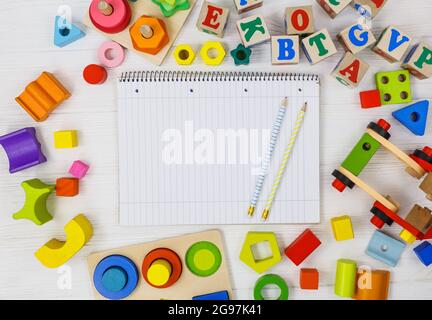 Open notepad, wooden rainbow, pencils, blocks on white wooden table. Back to school, education concept Stock Photo