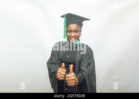Stock photo of an African female graduand or graduating students in her black graduation outfit and joyfully doing thumbs up gesture Stock Photo