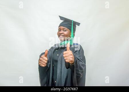 Stock photo of an African female graduand or graduating students in her black graduation outfit and joyfully doing thumbs up gesture Stock Photo
