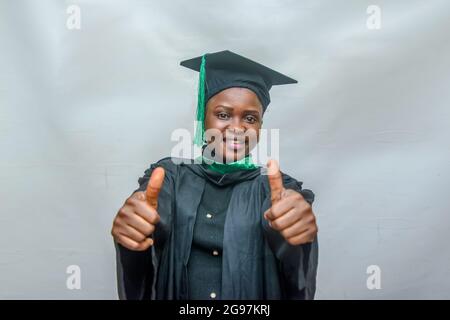 Stock photo of an African female graduand or graduating students in her black graduation outfit and joyfully doing thumbs up gesture Stock Photo