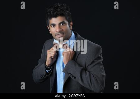 Close up portrait - Indian man ties a bowtie at the collar, correcting wood bow on his grey background Stock Photo