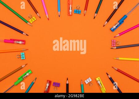 multi-colored pencils and pens forming a colored circle, isolated on an orange background Stock Photo
