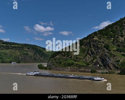 Beautiful landscape with Rhine river surrounded by rocky slopes with cargo barge passing by and excursion cruise ship in background on sunny day. Stock Photo