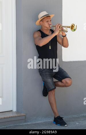 Latino man with a hat leaning on a wall playing the trumpet: Selective focus. Music concept. Stock Photo