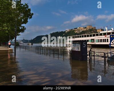 People looking at flooded river promenade in city Koblenz on Rhine riverbank with high water level in summer and fortress Ehrenbreitenstein. Stock Photo