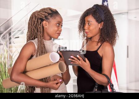 Two female office workers talking about work in office using digital tablet and phone Stock Photo