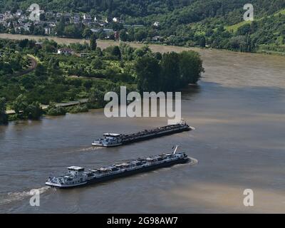 Two inland cargo ships sailing alongside on Rhive river, an important waterway, on sunny day with town Boppard in background and green trees in summer. Stock Photo