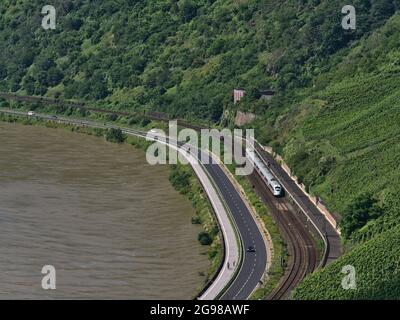 Aerial view of Rhine riverbank with railroad tracks and InterCity Express (ICE) train of Deutsche Bahn passing cars on adjacent street on sunny day. Stock Photo