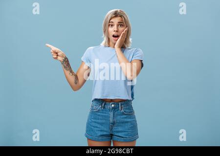 Waist-up shot of worried surprised emotive blonde woman in t-shirt saying gosh opening mouth from shock holding palm on cheek looking with empathy Stock Photo