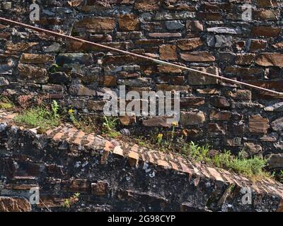 Front view of textured stone wall with ascending path and rusty metal railing with orange patterned bricks and weed in between near Boppard, Germany. Stock Photo