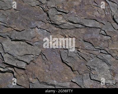Close-up view of slate (also shale, schist) with visible cracked layers and colored surface with raptures on sunny day with shadow pattern. Stock Photo