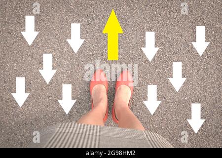 Businesswoman standing with orange shoes on street with one yellow arrow against other opposing direction white arrows. Stock Photo