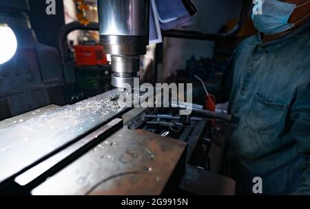 A man wear surgical mask working with milling machine. Tool for cut metal workpiece. Vertical milling machine with cemented carbide milling cutter. Stock Photo