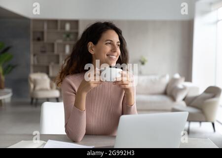 Smiling Latino woman drink coffee work on laptop Stock Photo