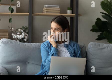 Pensive woman sit on sofa with laptop Stock Photo