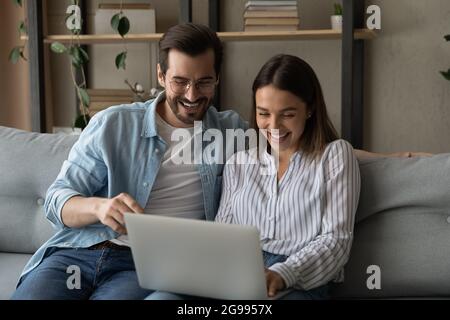 Laughing couple enjoy funny internet content while sit on sofa Stock Photo