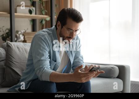 Man in glasses sit on sofa holding smartphone read messages Stock Photo