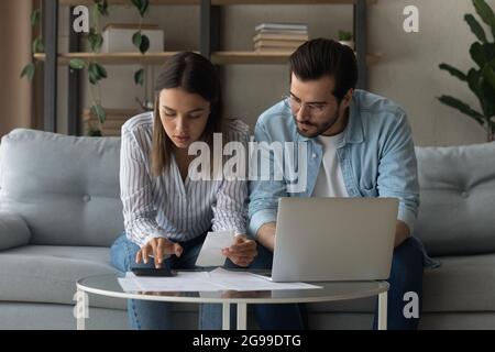 Serious millennial spouses calculate expenses sit on sofa at home Stock Photo