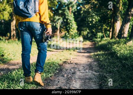 An unrecognizable man with backpack and boots trekking through the woods with a camera in his hand Stock Photo