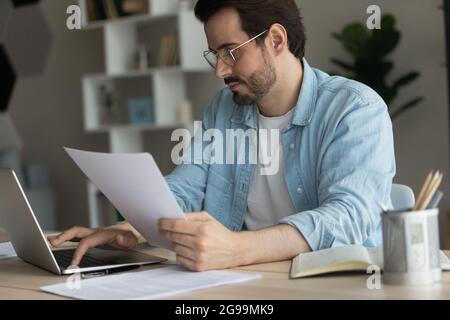Focused businessman doing paperwork working online on laptop Stock Photo