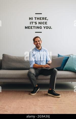 Confident executive sitting on sofa and using laptop. Happy man at lobby in office with laptop looking at camera. Stock Photo