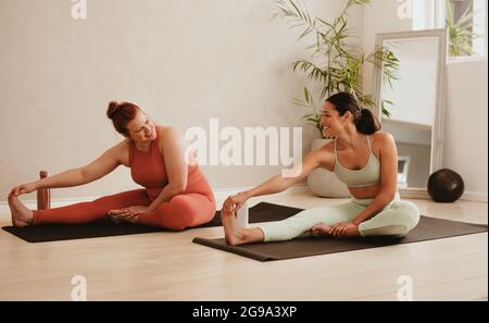 Two women doing stretching and yoga workout at gym. Female trainer with her student in physical training session. Stock Photo