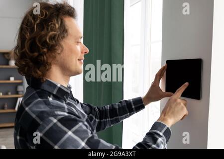Man Using Tablet On Wall With Smart Home Application Indoors Stock Photo