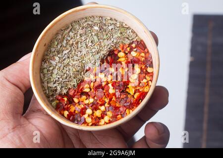 chili flakes and oregano bowl in hand isolated on light background Stock Photo