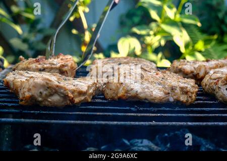 Frying juicy pieces of fresh pork neck steak meat prepared on grill or outdoor barbecue lattice in backyard. Smoke on charcoal. Selective focus.  Clos Stock Photo