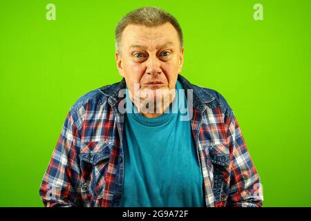 Sadness suffering, bewildered senior caucasian man in checkered shirt is experiencing pain, grief, loss. He disappointed. Green background. Close-up. Stock Photo