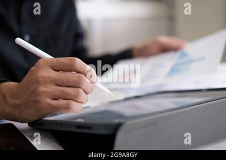 Closeup man with stylus pen writing on digital notepad, touching on digital tablet screen working on laptop computer in office. Web designer working h Stock Photo