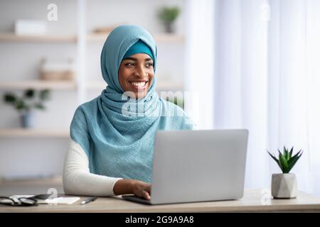 Remote Career. Happy Black Muslim Woman Sitting At Desk With Laptop Stock Photo