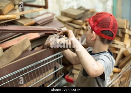 The child carries firewood. Firewood baskets. The boy collects fuel for heating. A child in an industrial area. Stock Photo