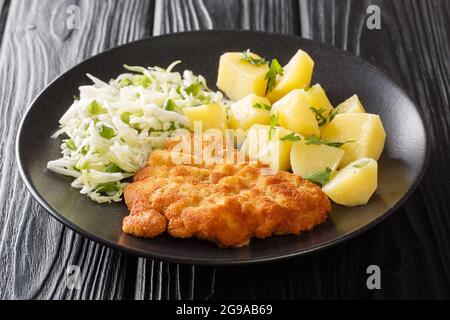 Kotlet Schabowy is a Polish pork schnitzel covered with breadcrumbs served with potatoes and fresh salad closeup in the plate on the wooden table. Hor Stock Photo