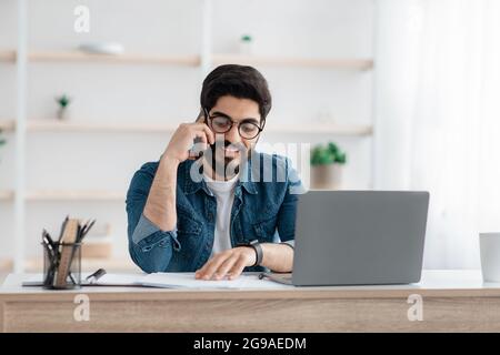 Young arab entrepreneur talking on cellphone and looking at documents, working with papers at home office, copy space Stock Photo