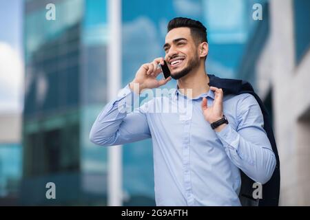Happy muslim entrepreneur going home from job, talking on cellphone Stock Photo