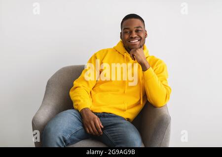 Black Man Posing Sitting In Armchair Posing Over Gray Background Stock Photo