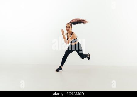 Front view of muscular woman running in studio against white wall Stock Photo