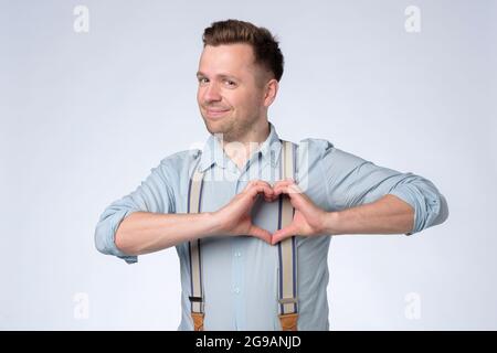 Smiling young man making heart gesture on his chest. Stock Photo