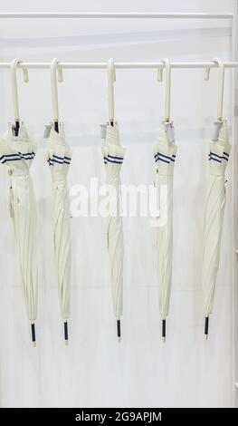 Five beige umbrellas hang on a coat hook hook, white background. Getting ready for the rainy season. Five modern umbrellas in a rack hanging in a whit Stock Photo