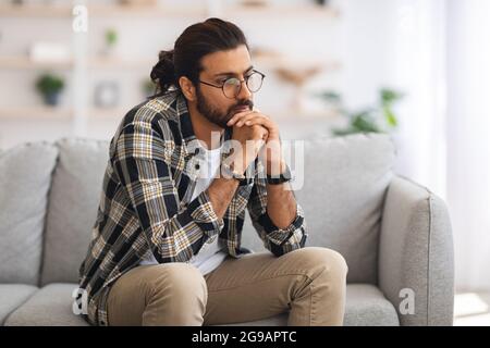 Pensive arab guy sitting on couch at home Stock Photo